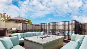 A patio with light blue cushioned seating, a fire pit, and a pool in the background.
