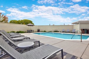 Zona de piscina con sillones de descanso y una mesa, rodeada por un muro bajo y vegetación.
