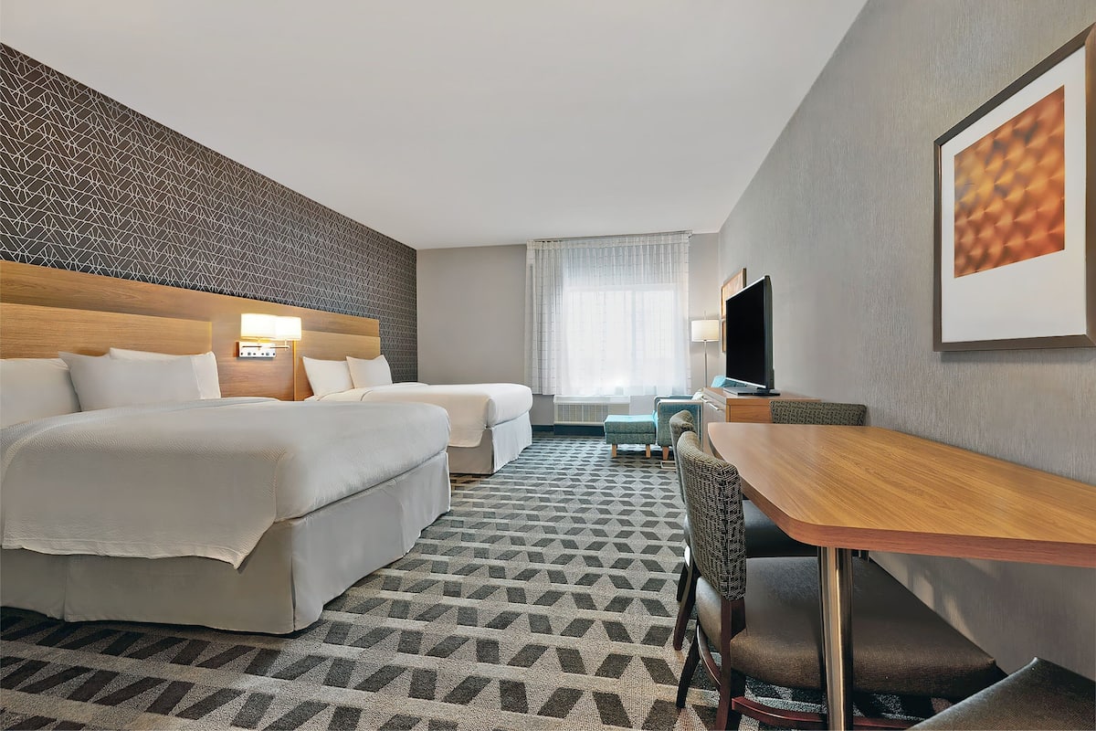 A hotel room with two beds, a wooden desk, a TV, and a patterned carpet.
