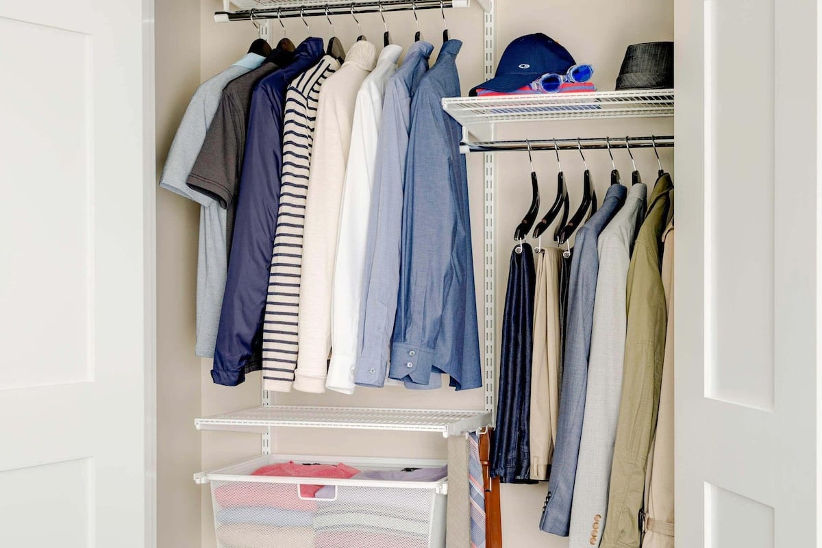 A walk-in closet with hanging clothes, shelves, and a suitcase.