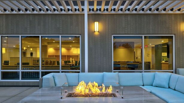 An outdoor seating area with a fire feature, large windows, and a modern building facade.