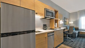 A modern kitchen with stainless steel appliances, wooden cabinetry, and a compact dining area with a chair and table.
