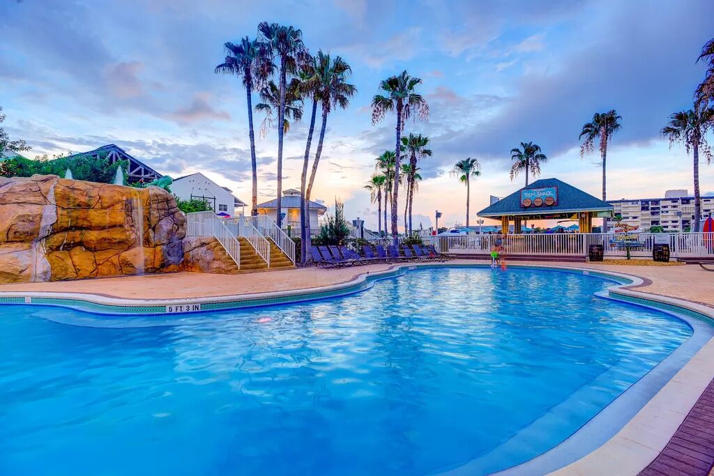 A swimming pool with a rock feature, palm trees, and a gazebo.