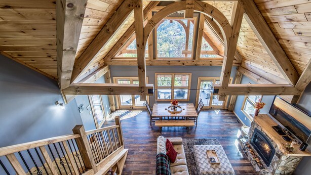 Ein geräumiger Loft mit hohen Decken, Holzbalken, einem Kamin aus Stein und großen Fenstern mit Blick ins Freie.