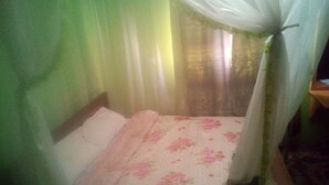 A single bed with a floral bedspread and a white pillow, a wooden headboard, and a canopy with sheer white curtains. - Desai Villa (Nairobi)