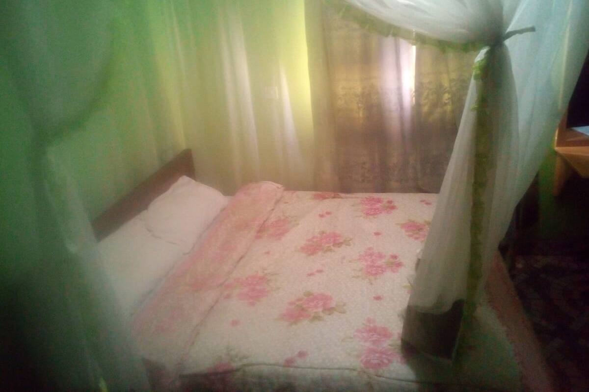 A single bed with a floral bedspread and a white pillow, a wooden headboard, and a canopy with sheer white curtains.