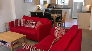 Un ambiente abitativo compatto con un divano rosso, un tavolino in legno e un'area pranzo con sedie e tavolo.
