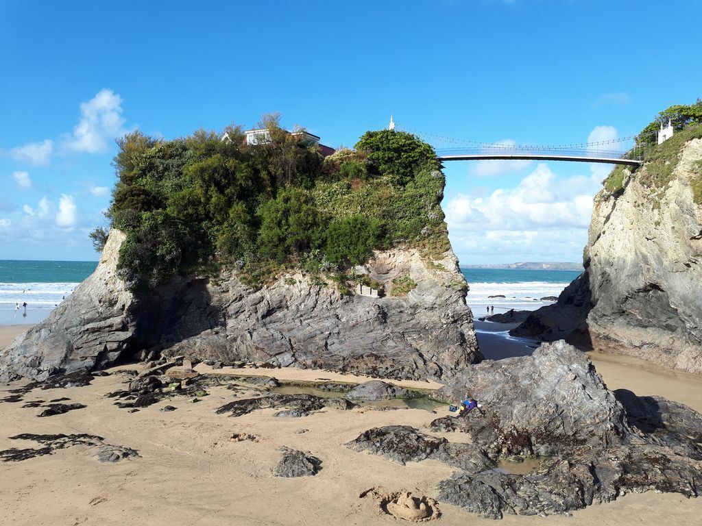 Una spiaggia con formazioni rocciose, un ponte e cielo sereno.