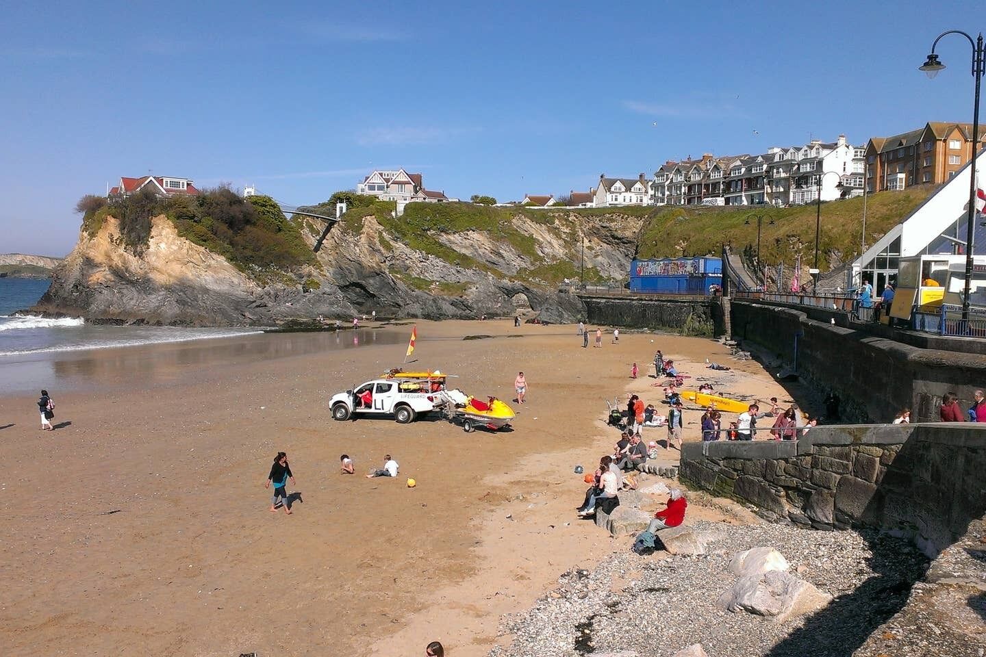 A beach with a lifeguard station, a white vehicle, and people enjoying the shore.