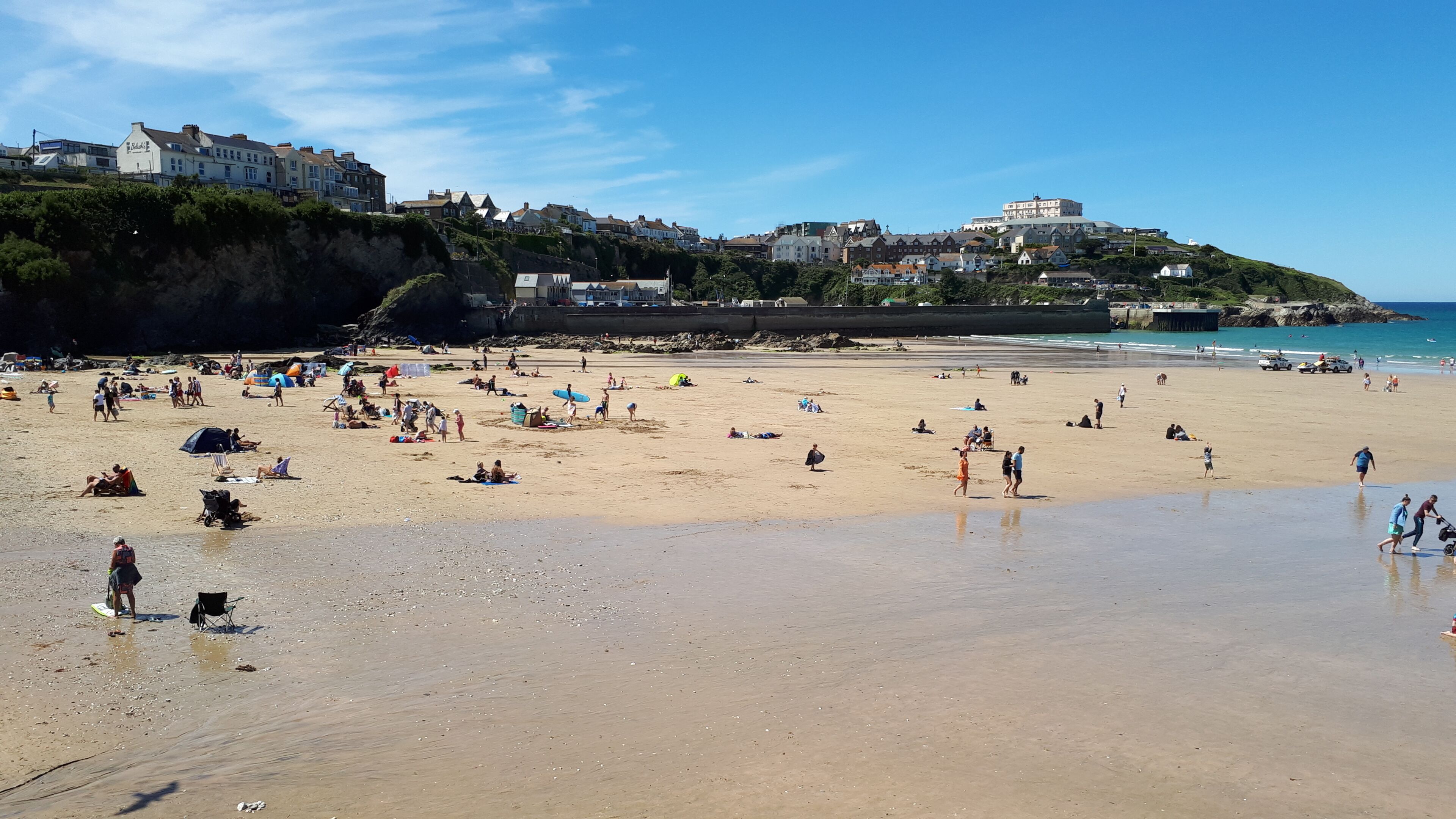 A beach with people, tents, and buildings in the background.