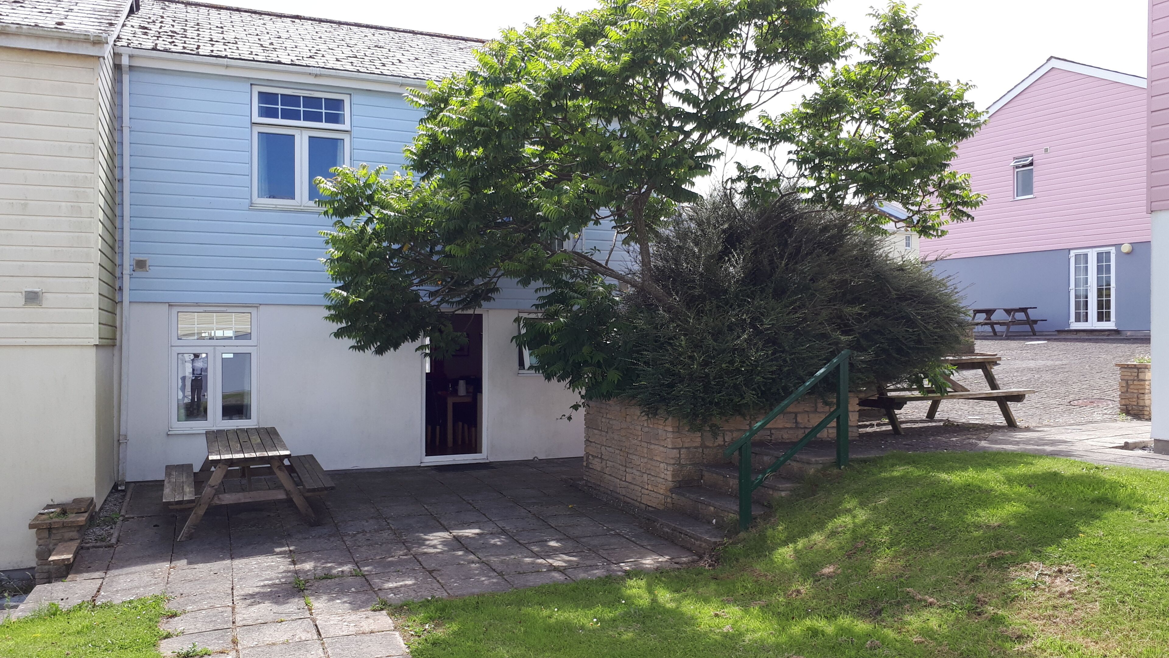 A residential property with a paved patio, a wooden bench, and a tree.