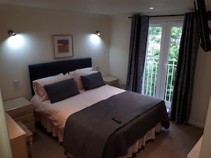 Une chambre d’hôtel avec un lit, des tables de chevet, une commode, un tableau encadré au mur et une fenêtre avec des rideaux.