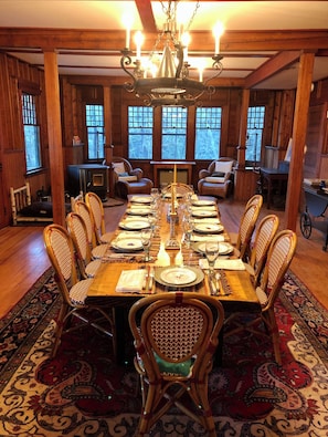 A dining room with a long wooden table set for a meal, surrounded by wicker chairs, and a chandelier above.