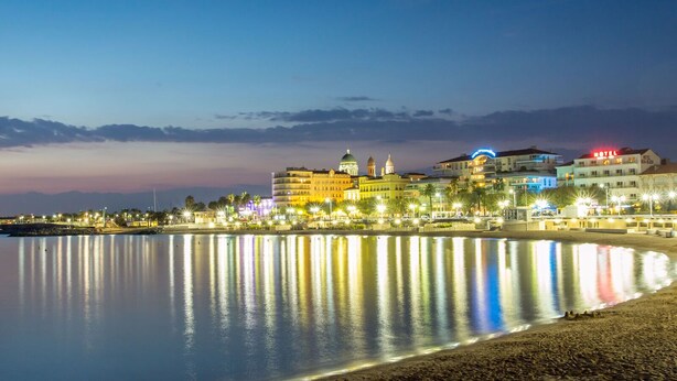 Un hotel costero con varias edificaciones, una playa y un mar tranquilo que refleja las luces.