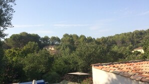 Una piscina con borde de baldosas, rodeada de vegetación y un edificio con techo de tejas.