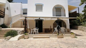Ein zweistöckiges Gebäude mit einer überdachten Terrasse, Sitzgelegenheiten im Freien und einer Treppe, die zum oberen Stockwerk führt.