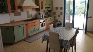 Eine kompakte Küche mit Gaskochfeld, Mikrowelle und Backofen, grünen Schränken sowie einem Essbereich mit Tisch und Stühlen.