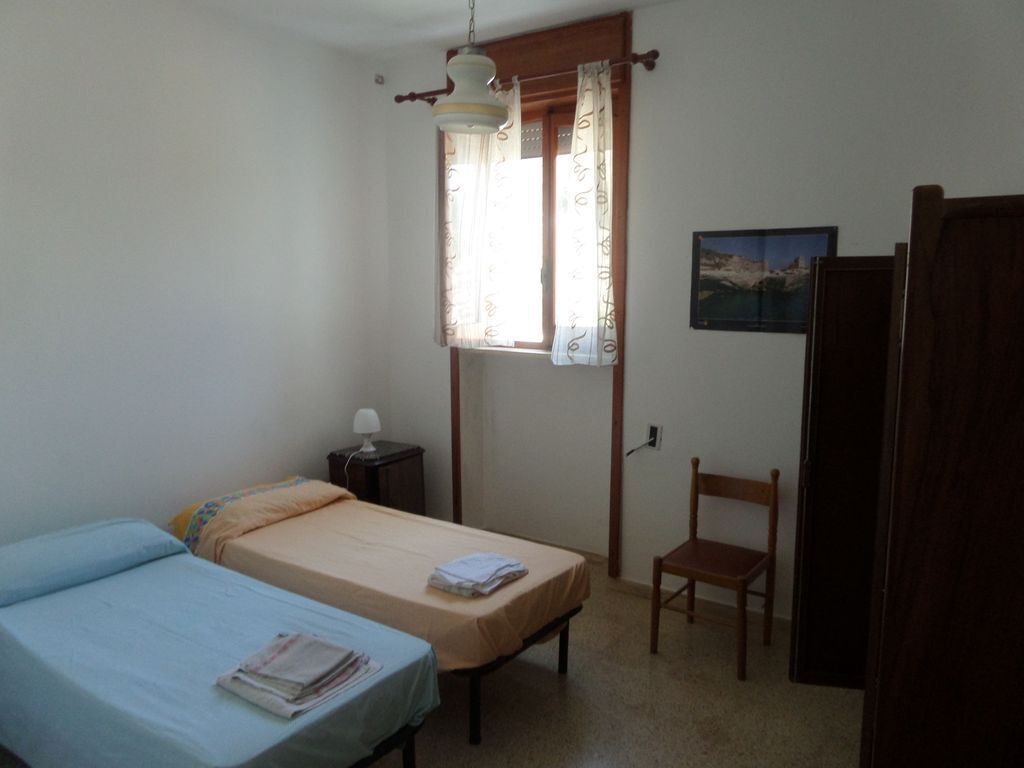 Ein Zimmer mit zwei Betten, einem Sessel, einem kleinen Tisch mit Lampe und einem Fenster mit Vorhängen.