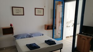 Ein Schlafzimmer mit einem Bett, zwei gerahmten Kunstwerken, einem Nachttisch, einem Fernseher und einer offenen Tür zu einem Badezimmer.
