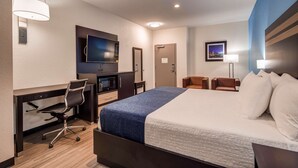 Quarto de hotel com cama, escrivaninha, cadeira, televisão e uma pequena cozinha equipada.