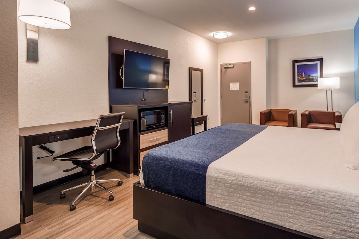 A hotel room with a bed, desk, chair, television, and a small kitchenette.