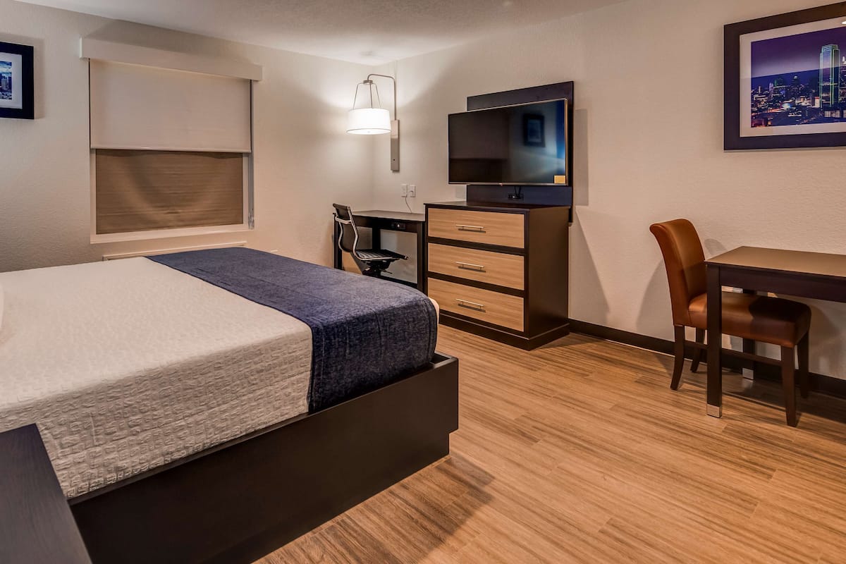 A hotel room with a bed, desk, chair, TV, and artwork on the walls.