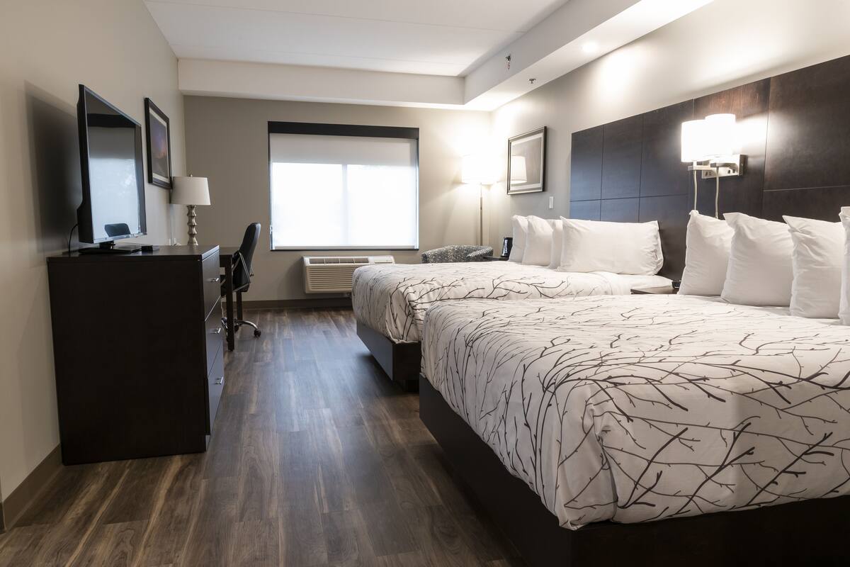 A hotel room with a large bed, a desk with a computer, a chair, and a window with blinds.