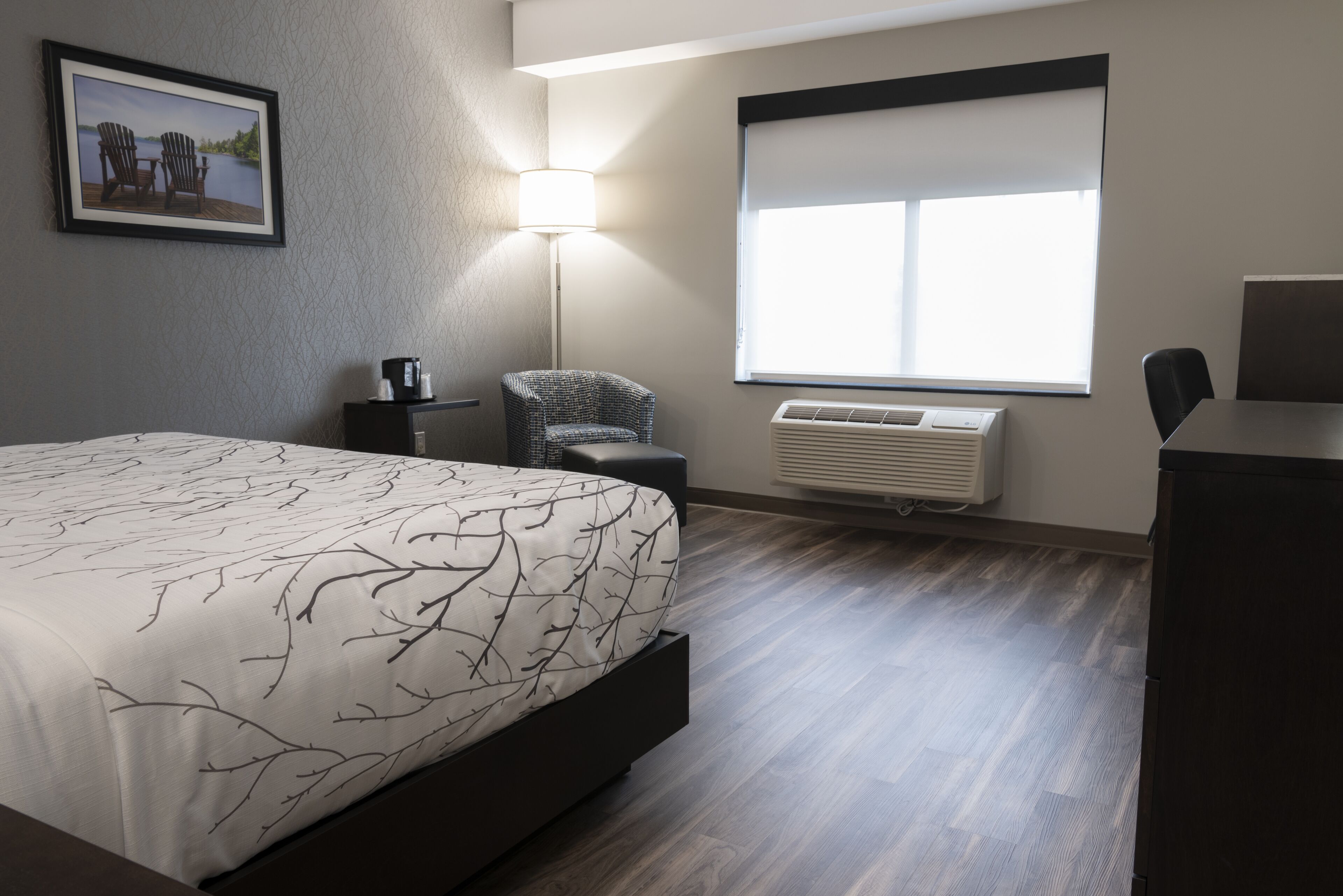 Quarto de hotel moderno com uma cama grande, uma escrivaninha, uma cadeira, um abajur e uma janela com vista.