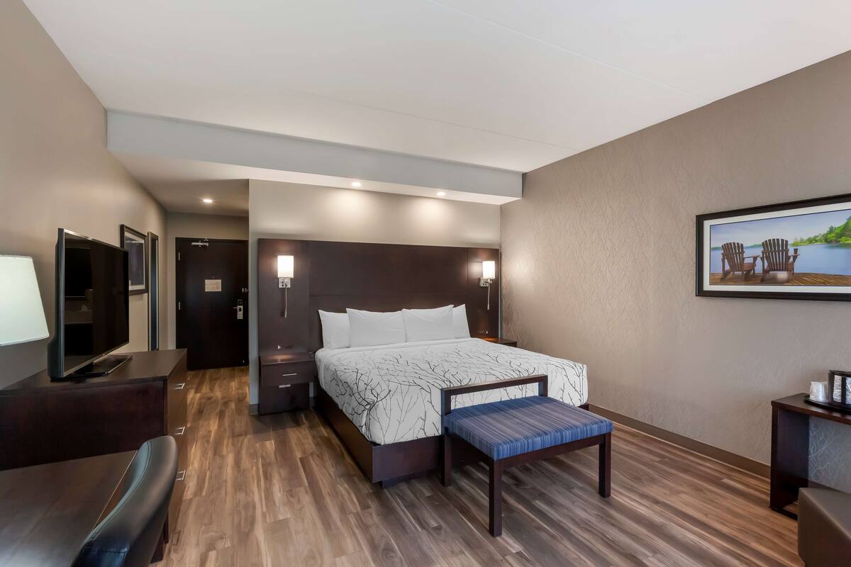 A hotel room with a bed, bedside tables, a TV, a desk, and a chair.