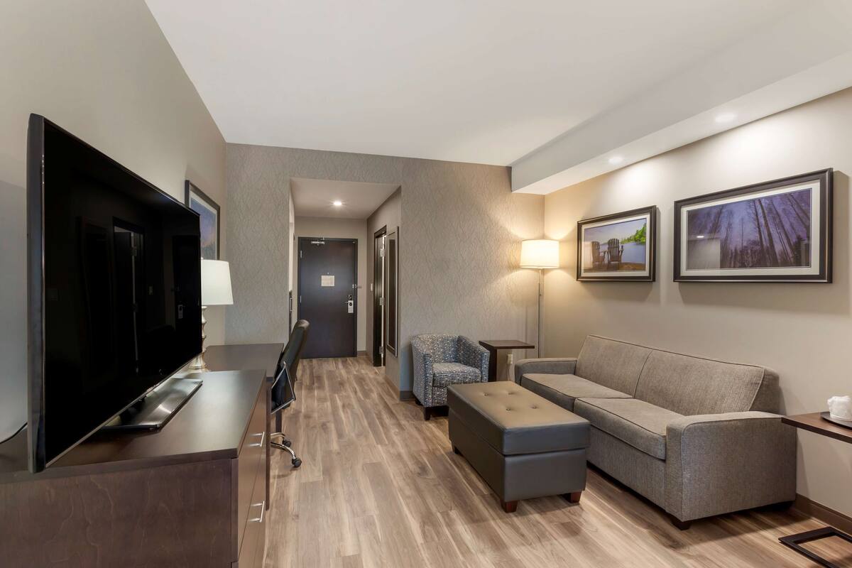 A hotel room with a flat-screen TV, a sofa, a chair, a coffee table, and two framed pictures on the wall.