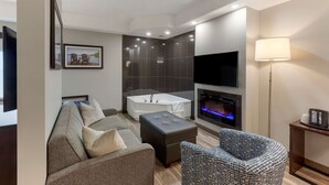 Una sala moderna con sofá, reposapiés y sillón estampado, un televisor de pantalla plana grande, una chimenea y una bañera.