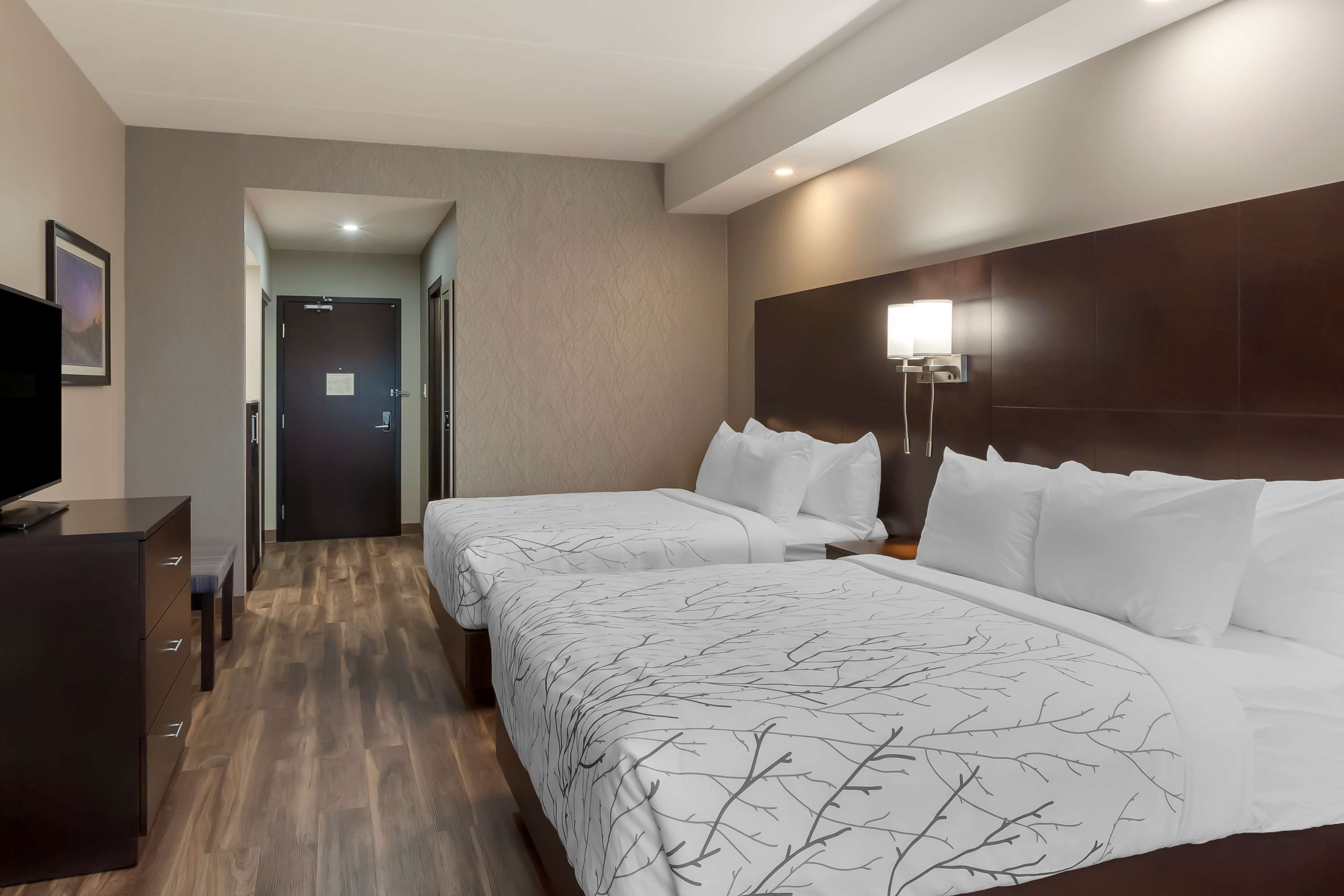A hotel room with two beds, a TV, a dresser, and a hallway leading to a door.