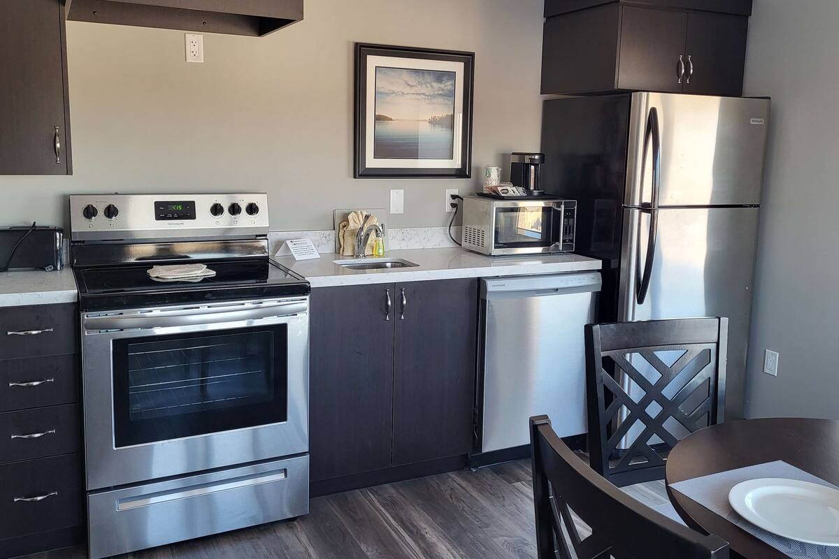 A modern kitchen with stainless steel appliances, dark cabinetry, and a dining area with a table and chairs.
