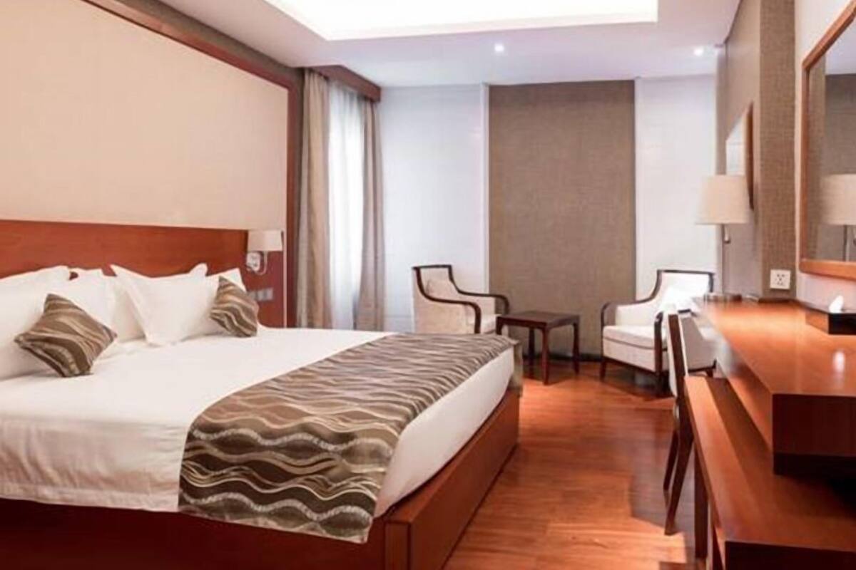 A hotel room with a large bed, a small table, two chairs, a desk, and a mirror.