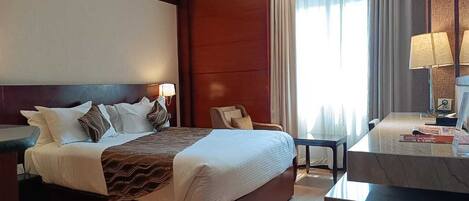 Een hotelkamer met een groot bed, een bureau, een stoel en een raam met gordijnen.