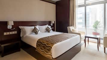 Una habitación de hotel con una cama grande, mesitas de noche, una silla, una pequeña mesa y una ventana con vistas a edificios.