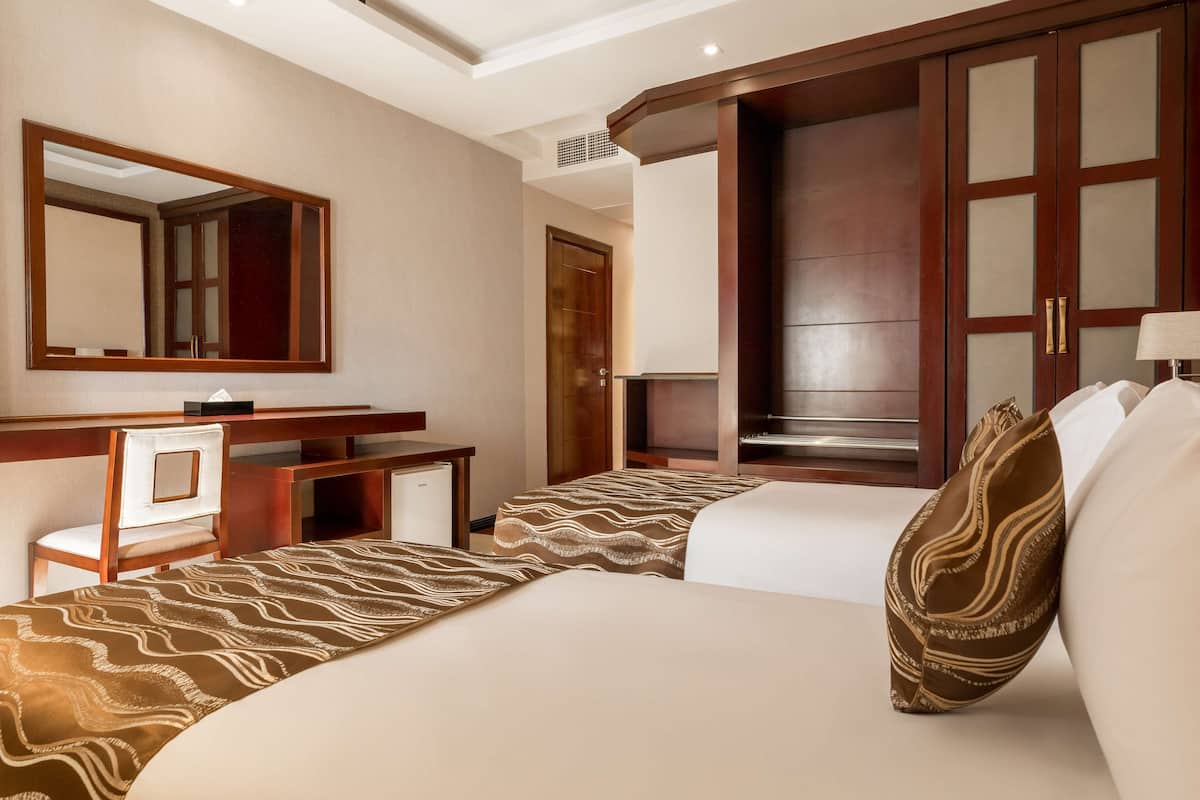 A hotel room with two beds, a desk, a chair, a large mirror, and a wardrobe.