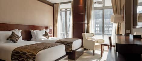 Une chambre d’hôtel avec deux lits, un bureau, une chaise et de grandes fenêtres.