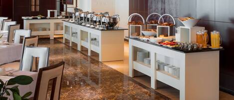 A buffet setup with various food items and beverages, a marble floor, and white furniture.