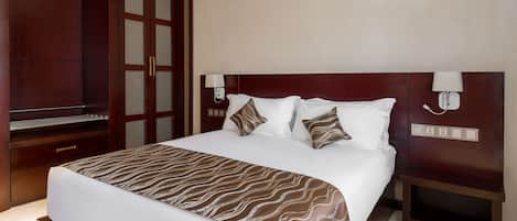 A hotel room with a large bed, wooden headboard, two bedside tables, and a wardrobe.