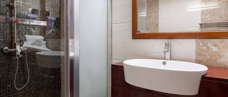 A modern bathroom with a glass shower enclosure, a white sink, and a wooden vanity.