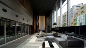 A modern lounge area with a mix of seating options, including sofas and a long bench, and a glass wall offering a view of the city. - Best Western Plus Fukuoka Tenjin-minami (Fukuoka)