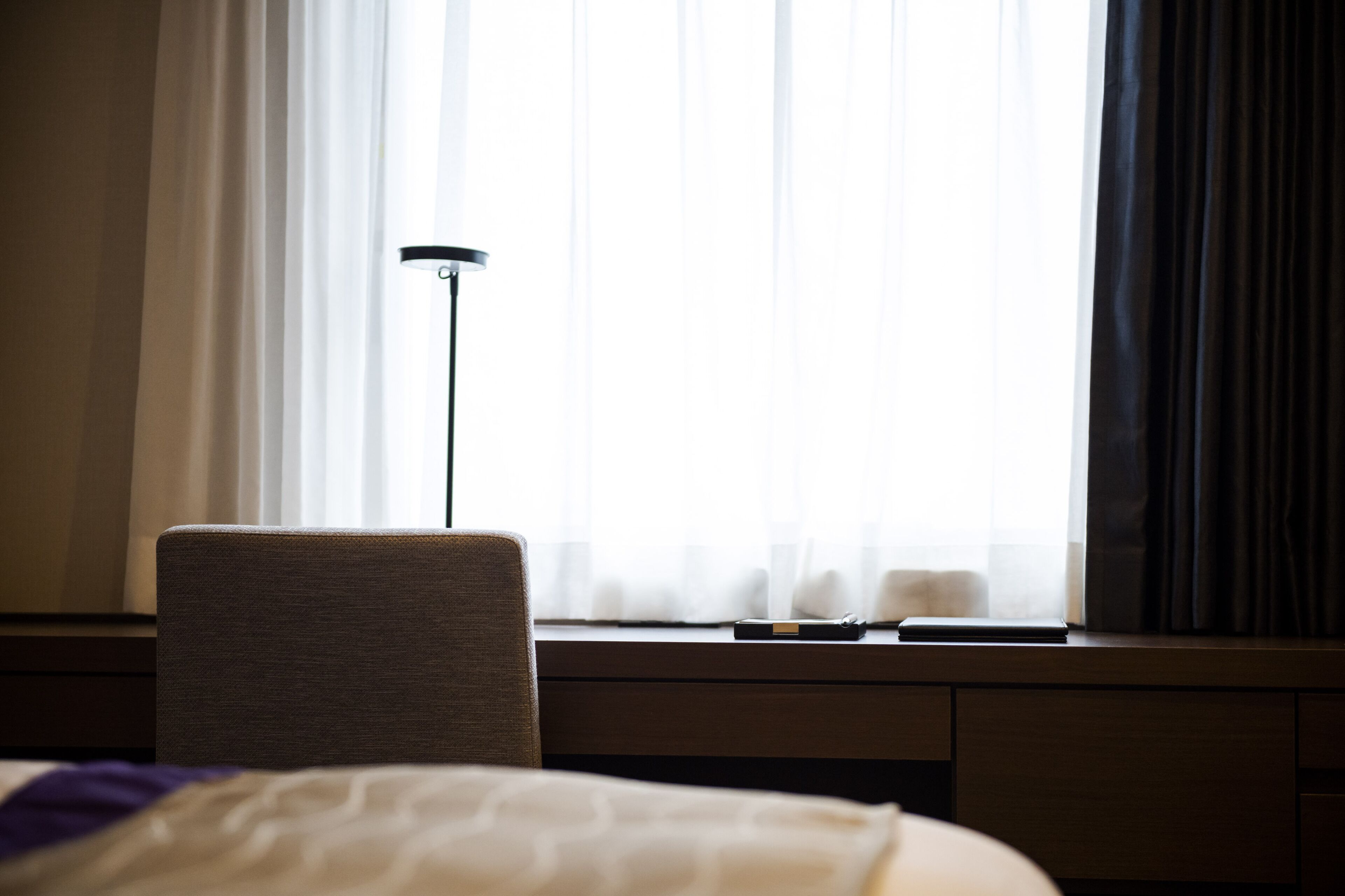 A hotel room with a bed, a desk, and a lamp.