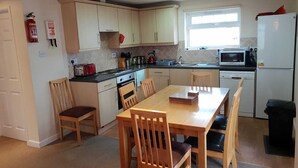 A compact kitchen with a dining table, chairs, a stove, a microwave, and a refrigerator.