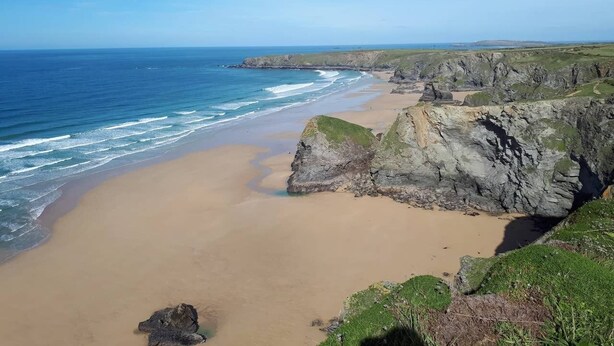 A coastal landscape with a sandy beach, rocky cliffs, and the ocean.