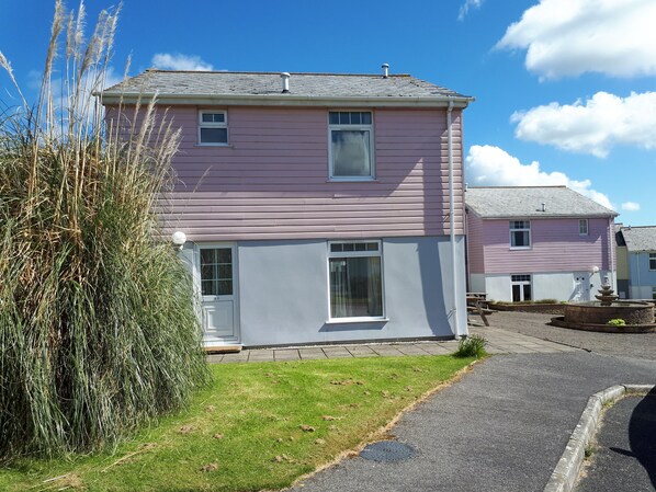 A two-story pink house with a front door, a small porch, and a visible window.