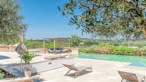 Un espace aménagé au bord de la piscine, avec des chaises longues, une pergola et une vue sur le paysage.