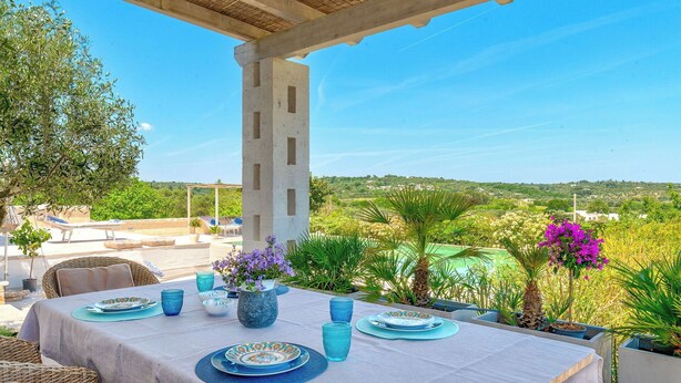 Un espace de restauration en plein air avec une table dressée pour quatre personnes, entouré de verdure et offrant une vue dégagée sur le paysage.