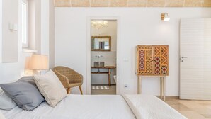 Une chambre à coucher comprenant un lit, une chaise, une armoire et une salle de bain visible à travers une porte ouverte.