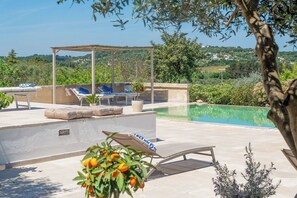 An outdoor pool area with lounge chairs, a pergola, and a view of the surrounding landscape.